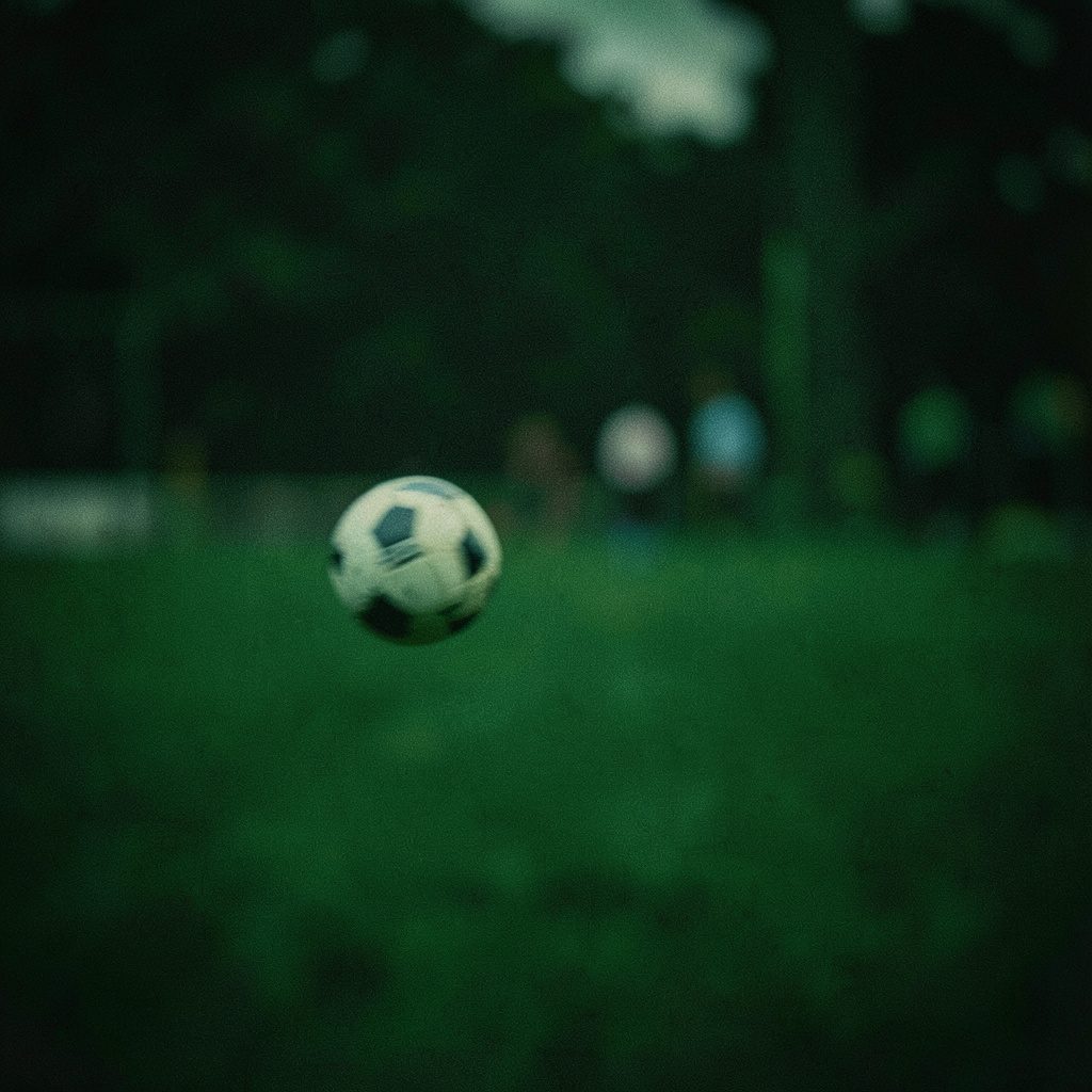 Yeşil çim bir futbol sahasını akşam ışıklandırmasıyla gösteren, koyu yeşil ve sarı tonlarda heyecanlı bir spor atmosferi taşıyan geniş sinematik kare.